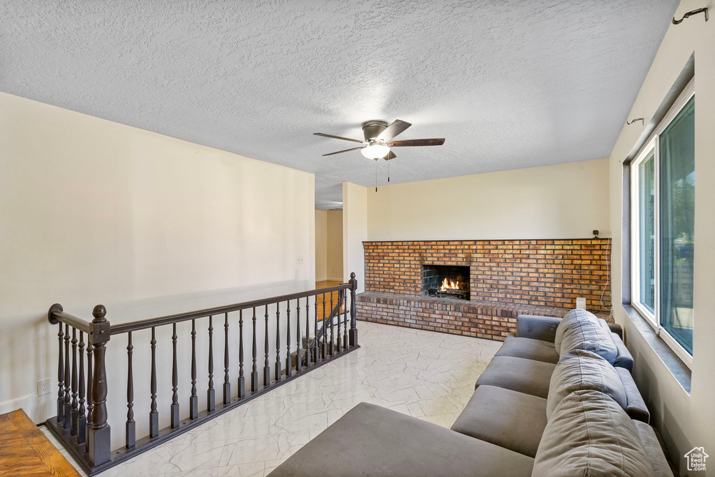 Living room featuring a ceiling fan, a brick fireplace, marble finish flooring, and a textured ceiling