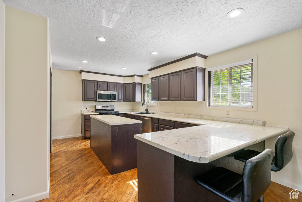 Kitchen with stainless steel appliances, baseboards, a center island, light wood-style flooring, and a peninsula