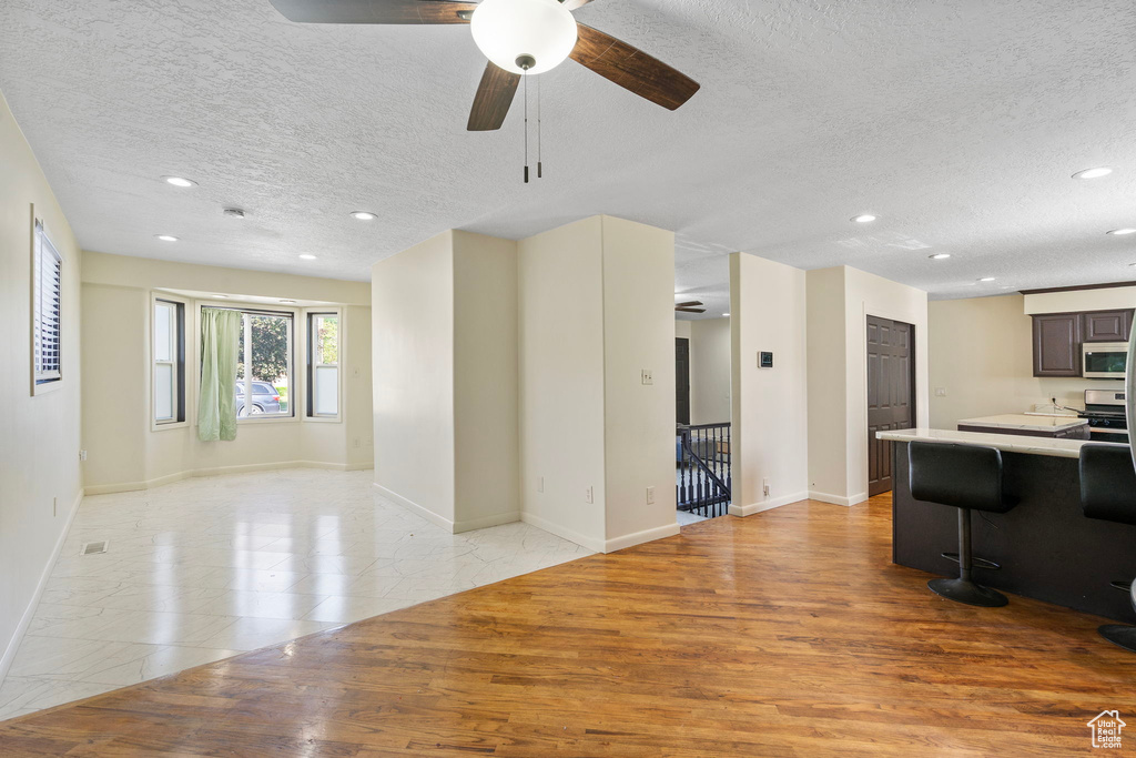 Living room featuring a textured ceiling, ceiling fan, recessed lighting, light wood finished floors, and baseboards