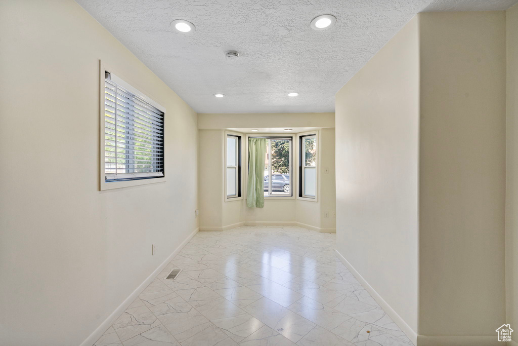 Spare room with light marble finish floors, plenty of natural light, a textured ceiling, baseboards, and recessed lighting