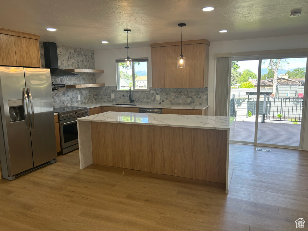 Kitchen with stainless steel appliances, wall chimney exhaust hood, a sink, light wood-type flooring, and backsplash