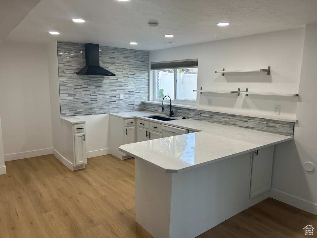 Kitchen with wall chimney exhaust hood, a sink, a peninsula, tasteful backsplash, and recessed lighting