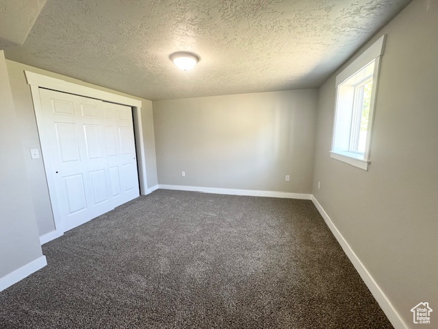 Unfurnished bedroom featuring a textured ceiling, dark carpet, baseboards, and a closet