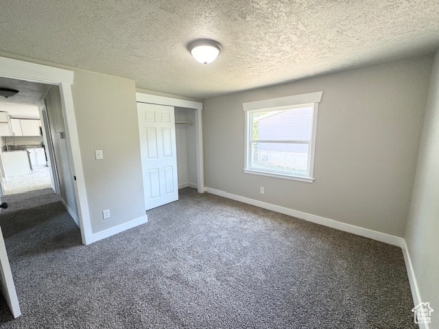 Unfurnished bedroom with dark carpet, a textured ceiling, baseboards, and a closet