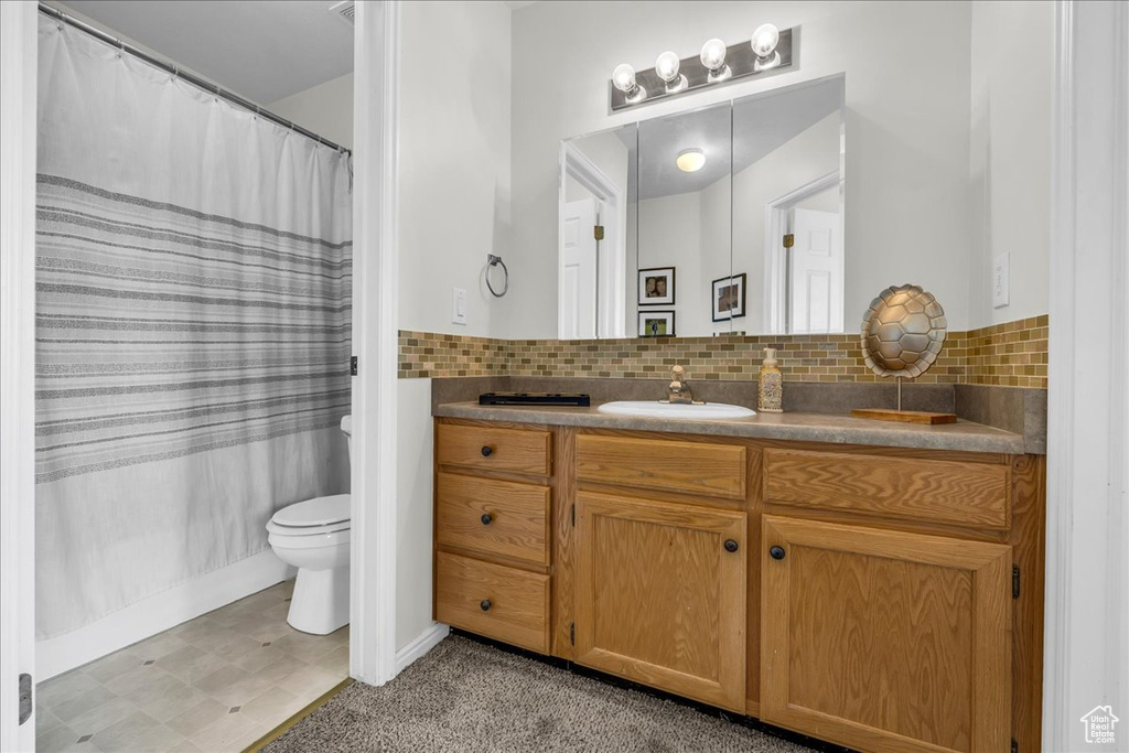 Bathroom featuring vanity, toilet, baseboards, tile patterned floors, and decorative backsplash