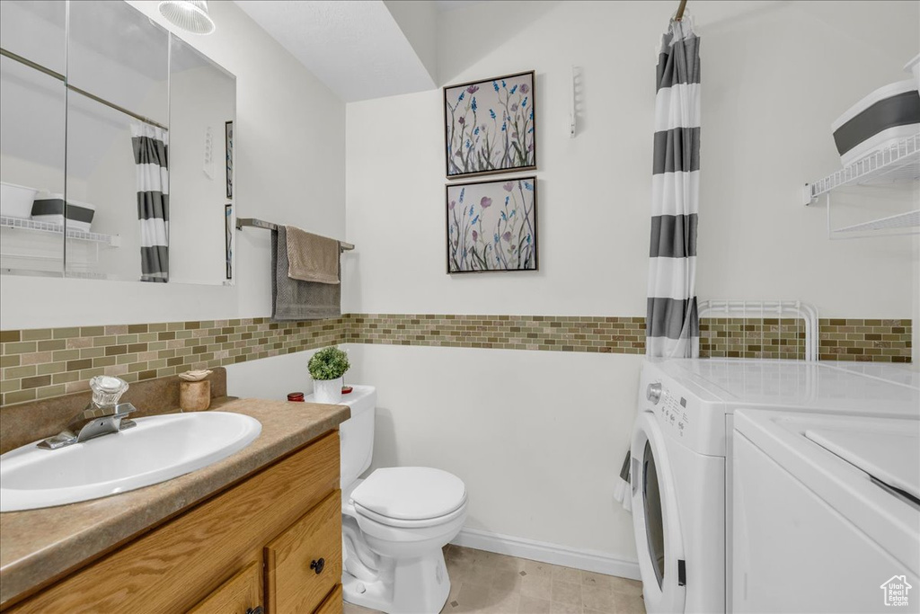 Bathroom with washing machine and clothes dryer, vanity, toilet, and decorative backsplash