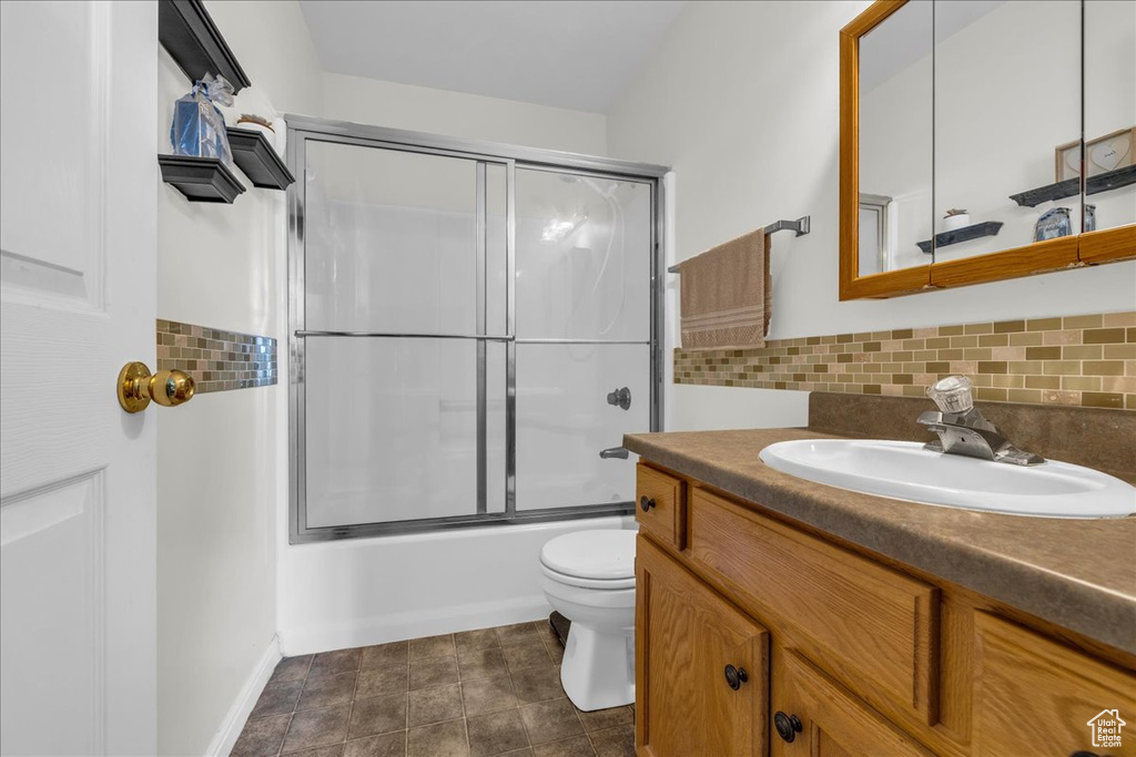 Bathroom featuring vanity, toilet, tasteful backsplash, shower / bath combination with glass door, and baseboards