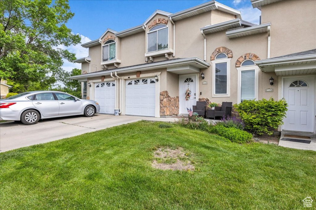 Townhome / multi-family property with concrete driveway, an attached garage, stucco siding, and a front lawn