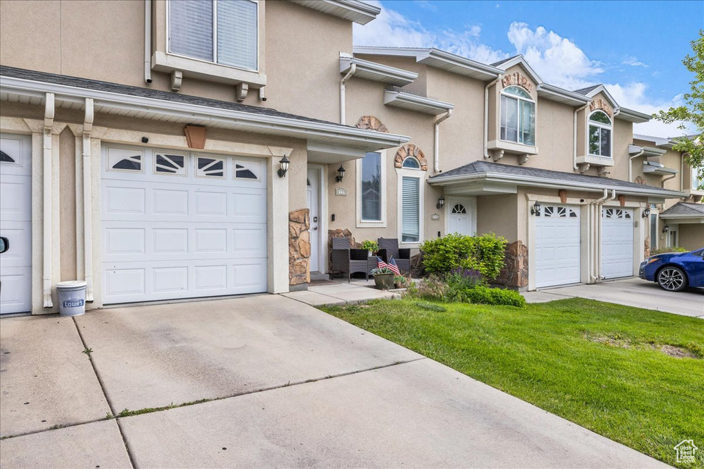 Multi unit property featuring a garage, driveway, stucco siding, and a front yard