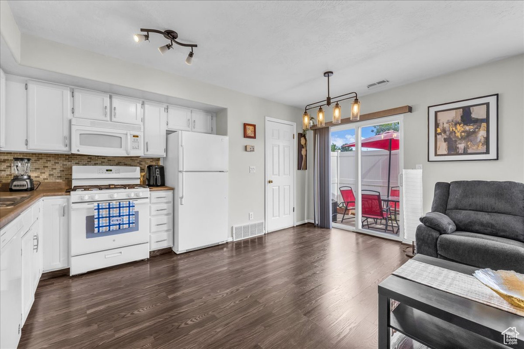 Kitchen featuring white appliances, open floor plan, a chandelier, dark wood finished floors, and white cabinetry