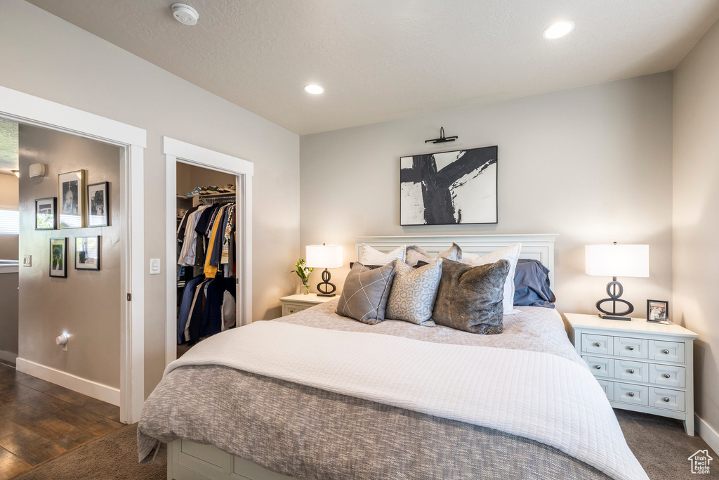 Bedroom featuring baseboards, a walk in closet, recessed lighting, a closet, and dark wood-type flooring