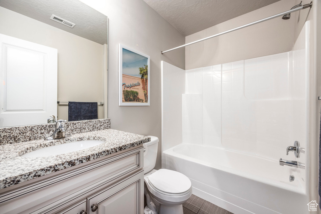 Full bath featuring toilet, bathtub / shower combination, vanity, and a textured ceiling