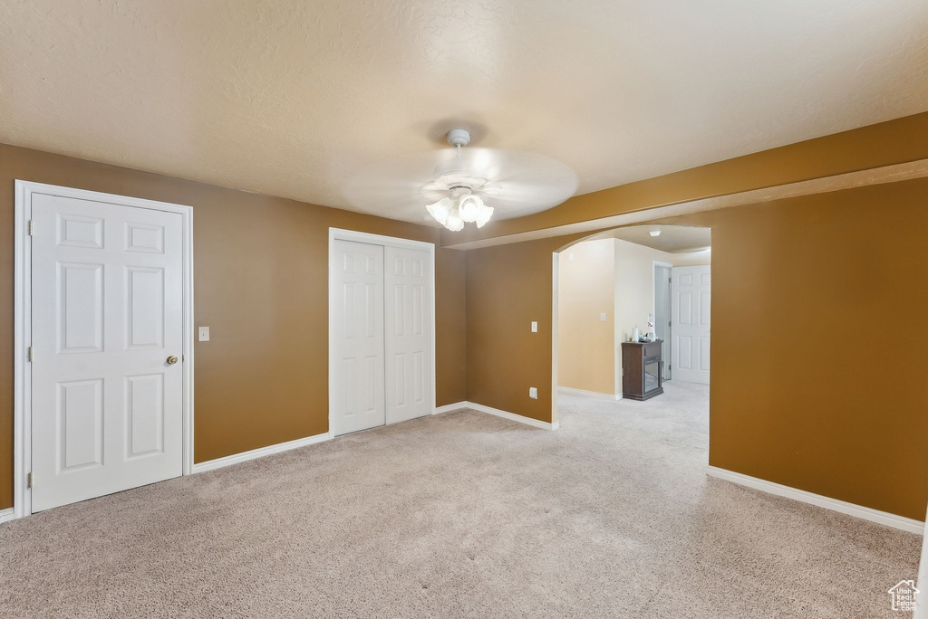 Unfurnished bedroom featuring arched walkways, light colored carpet, baseboards, and a closet