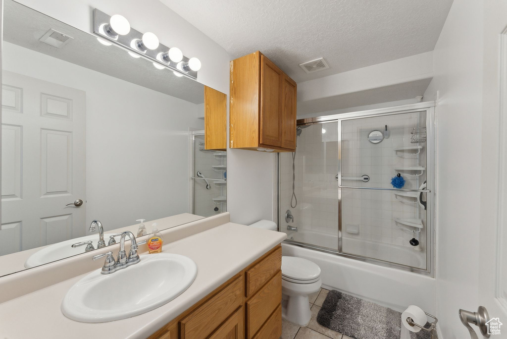 Bathroom featuring toilet, vanity, tile patterned floors, shower / bath combination with glass door, and a textured ceiling