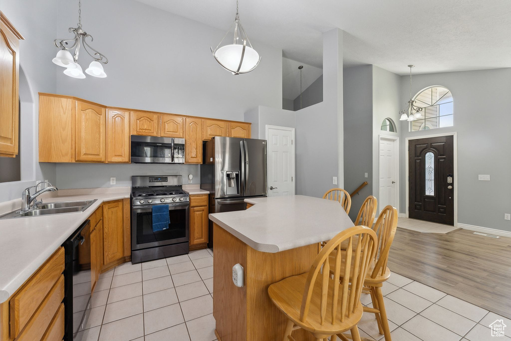 Kitchen with appliances with stainless steel finishes, high vaulted ceiling, light tile patterned floors, a sink, and light countertops