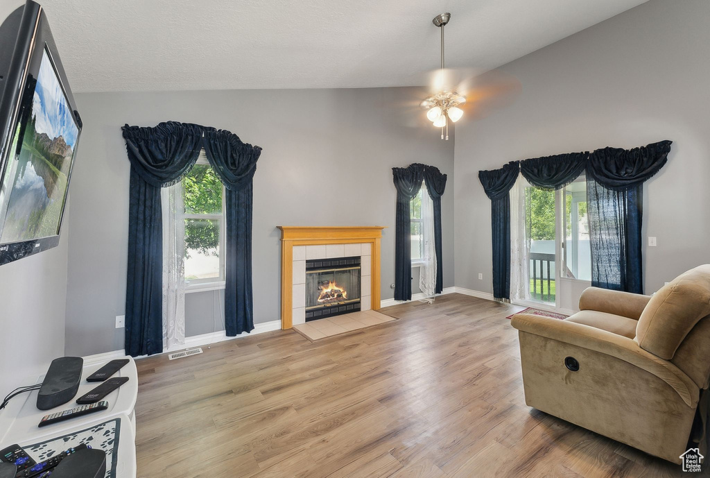 Living area featuring vaulted ceiling, healthy amount of natural light, ceiling fan, a tiled fireplace, and wood finished floors