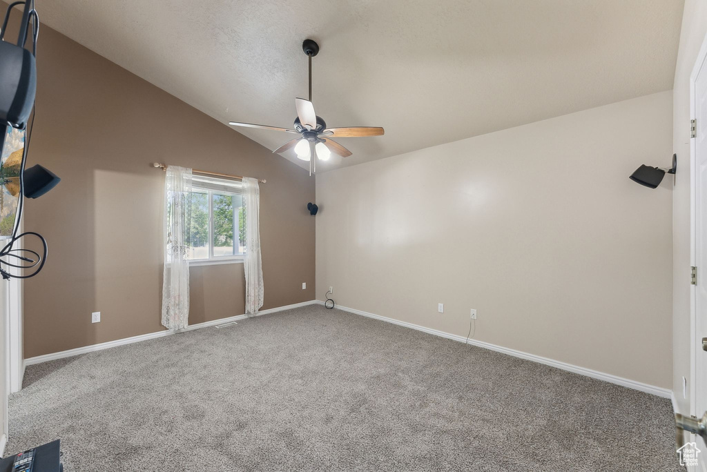 Empty room featuring a ceiling fan, carpet, vaulted ceiling, and baseboards