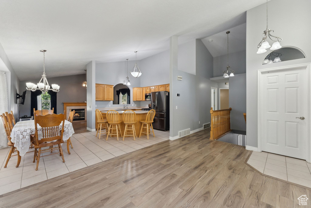Dining space with a chandelier, light wood-style flooring, high vaulted ceiling, a tiled fireplace, and baseboards