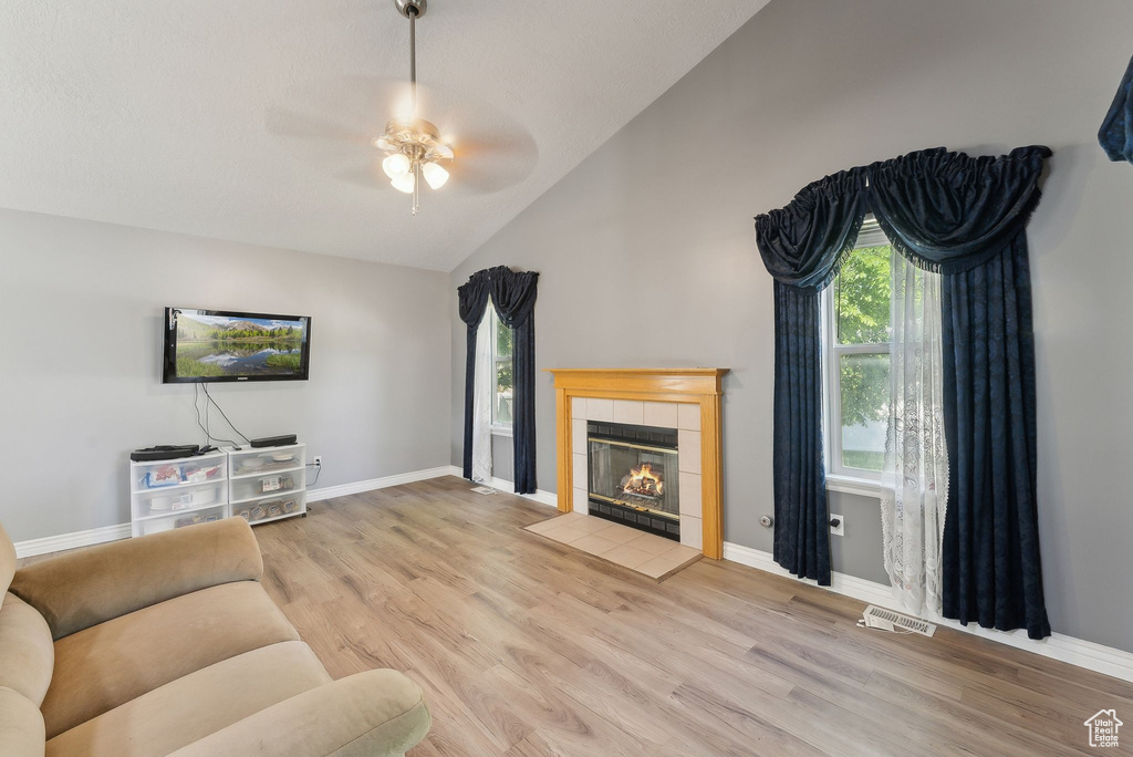 Living room with ceiling fan, plenty of natural light, wood finished floors, a tile fireplace, and high vaulted ceiling