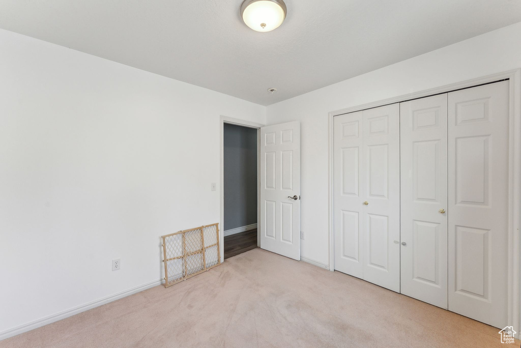 Unfurnished bedroom with light carpet, baseboards, and a closet
