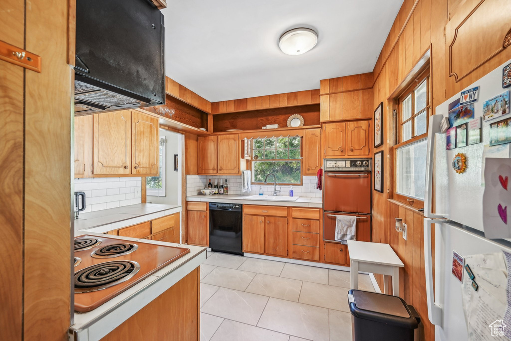 Kitchen featuring freestanding refrigerator, black dishwasher, a sink, backsplash, and double wall oven