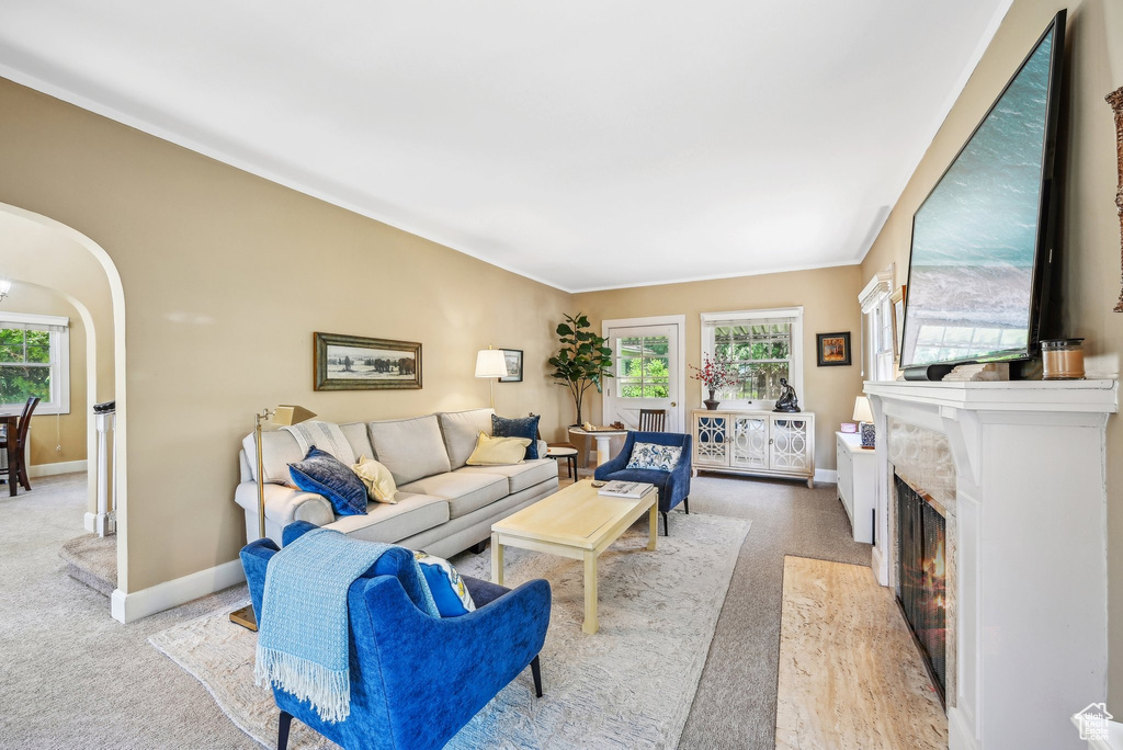 Living room with light carpet, baseboards, arched walkways, and a lit fireplace