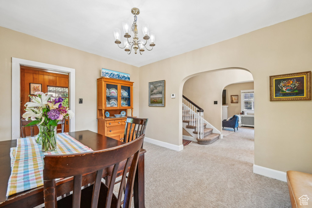 Dining room featuring arched walkways, carpet, a chandelier, baseboards, and stairs