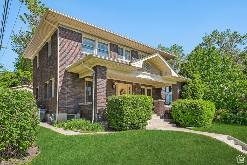 View of front of home with a front yard, covered porch, and brick siding