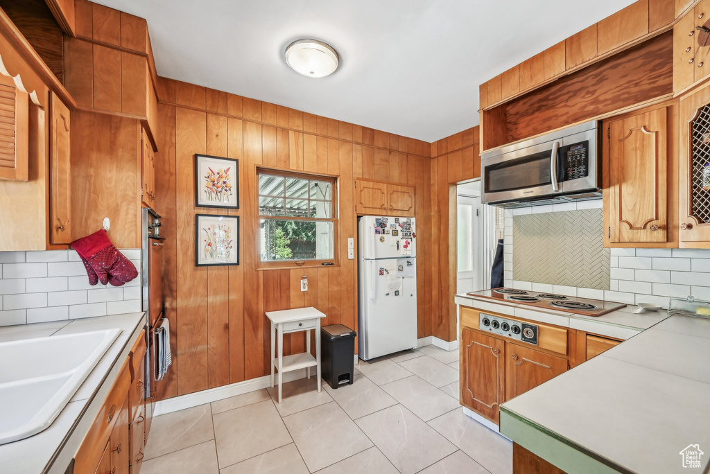 Kitchen featuring freestanding refrigerator, stainless steel microwave, electric stovetop, tasteful backsplash, and light countertops
