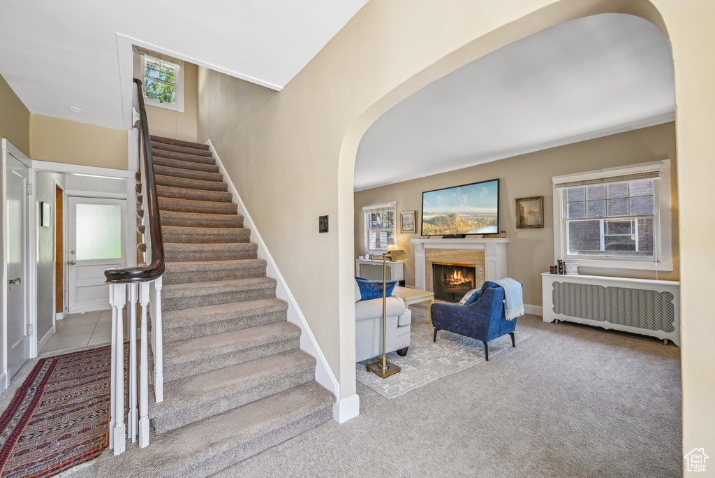 Staircase featuring radiator heating unit, arched walkways, healthy amount of natural light, and a lit fireplace