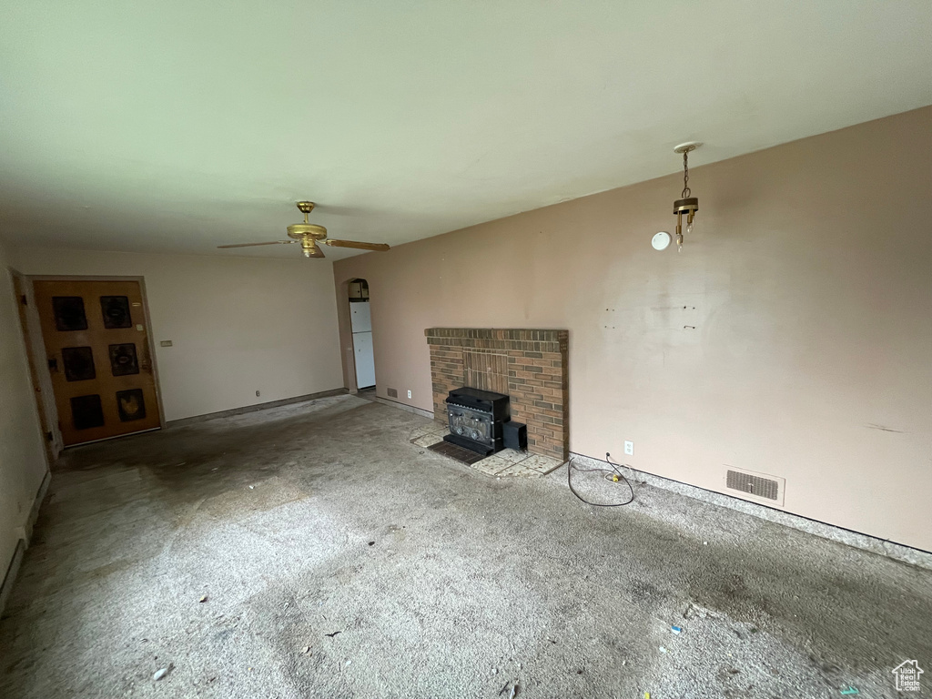 Unfurnished living room with a wood stove, carpet, a ceiling fan, and baseboards