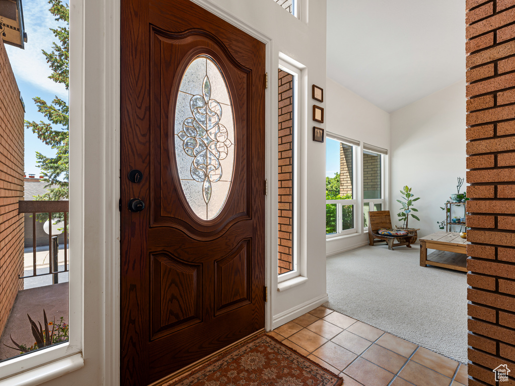 Foyer entrance featuring light carpet, healthy amount of natural light, light tile patterned floors, and baseboards
