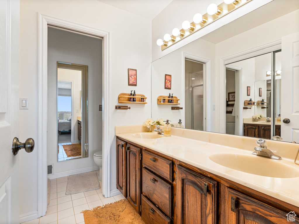 Ensuite bathroom featuring toilet, double vanity, tile patterned floors, an enclosed shower, and baseboards