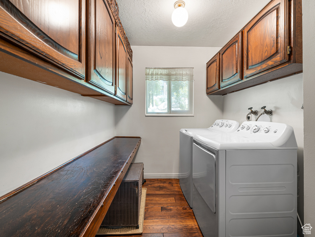 Laundry area featuring cabinet space, dark wood-type flooring, separate washer and dryer, baseboards, and a textured ceiling