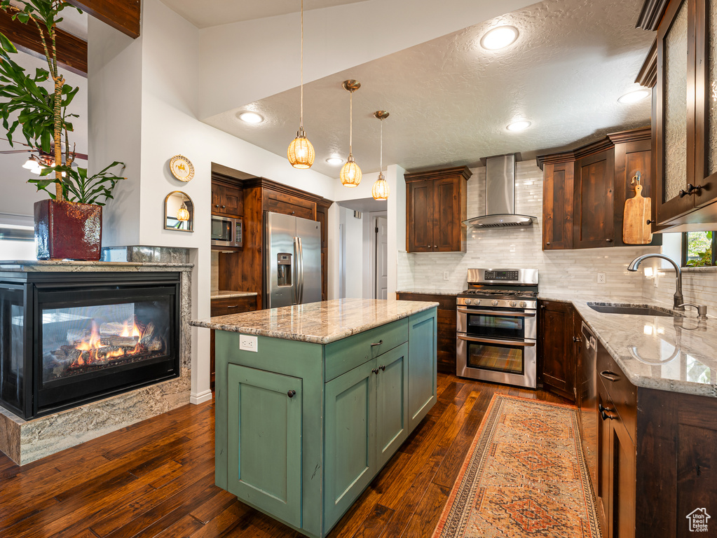 Kitchen featuring wall chimney range hood, appliances with stainless steel finishes, green cabinets, a sink, and backsplash