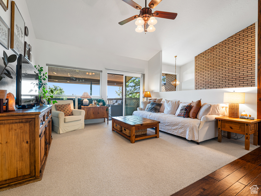 Living room featuring vaulted ceiling, ceiling fan, brick wall, and wood finished floors