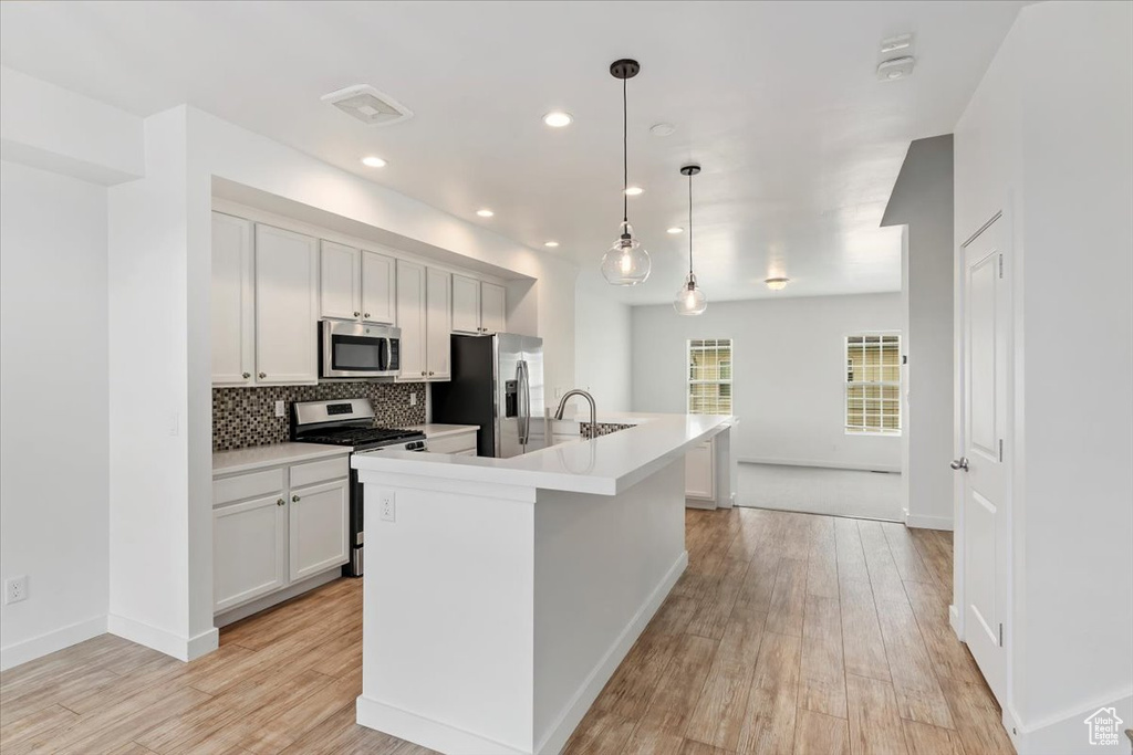 Kitchen with stainless steel appliances, light wood-style flooring, backsplash, a kitchen island with sink, and recessed lighting
