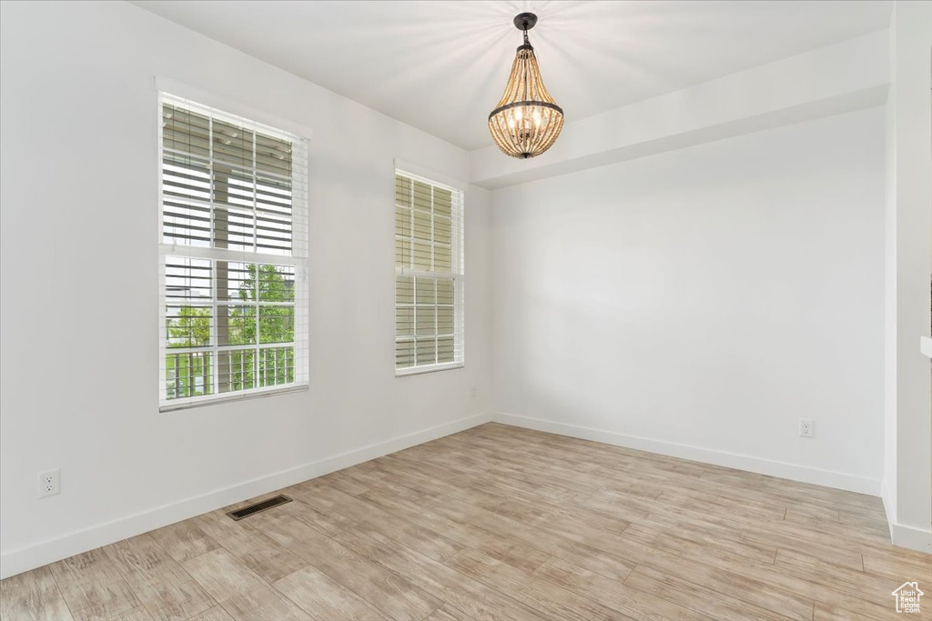 Empty room featuring a chandelier, light wood-style flooring, and baseboards