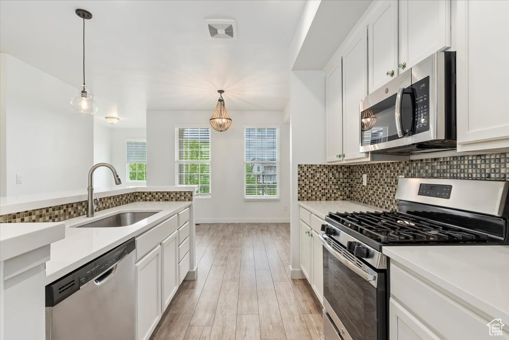 Kitchen featuring stainless steel appliances, a sink, backsplash, white cabinetry, and pendant lighting