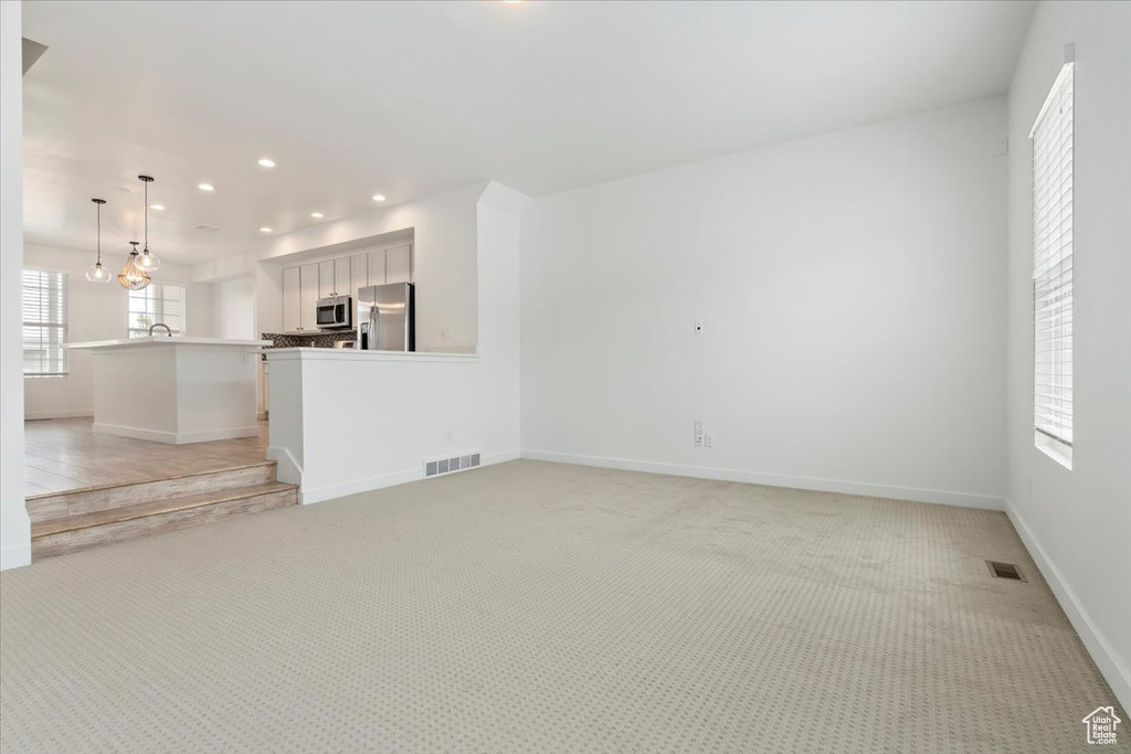 Unfurnished living room featuring recessed lighting, light colored carpet, baseboards, and a sink
