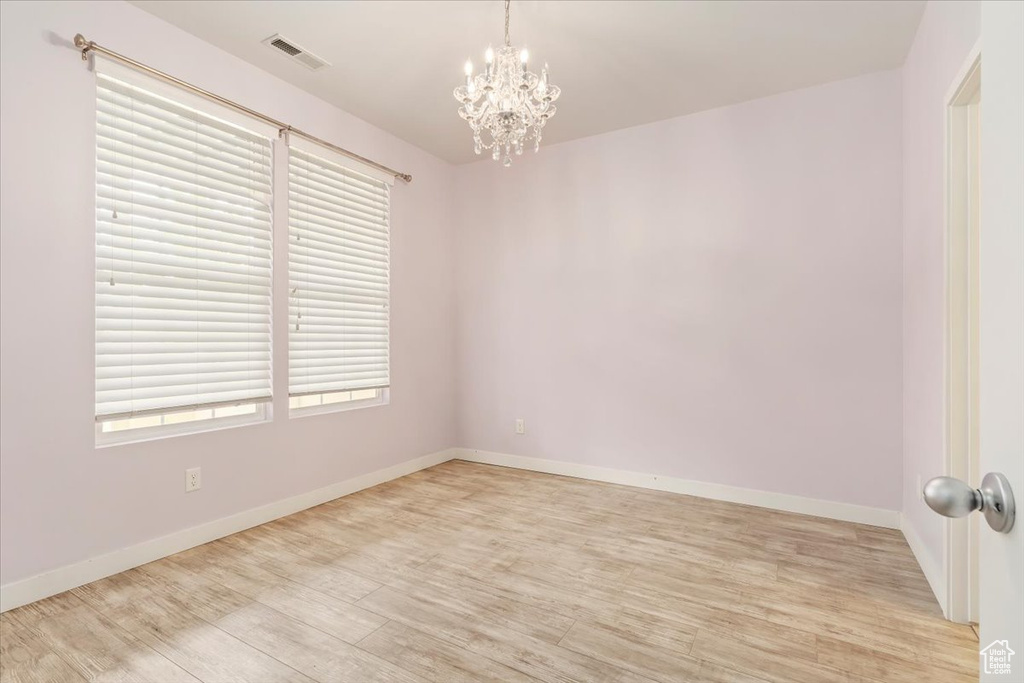 Spare room featuring a chandelier, light wood-style flooring, and baseboards
