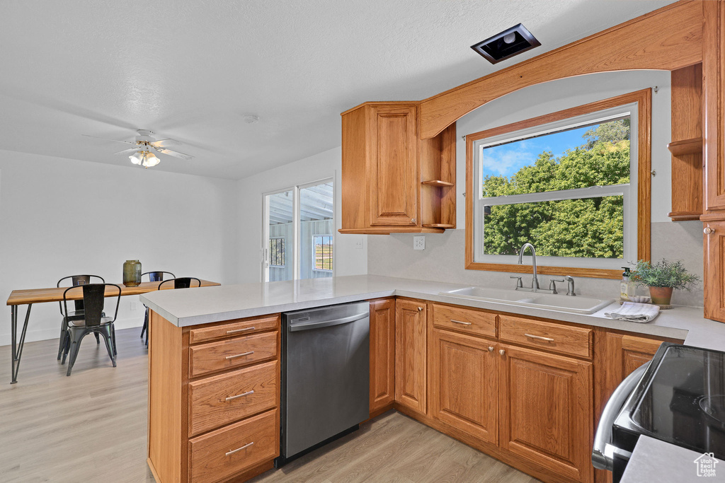 Kitchen featuring stainless steel dishwasher, black range with electric cooktop, a peninsula, light wood-style flooring, and a sink