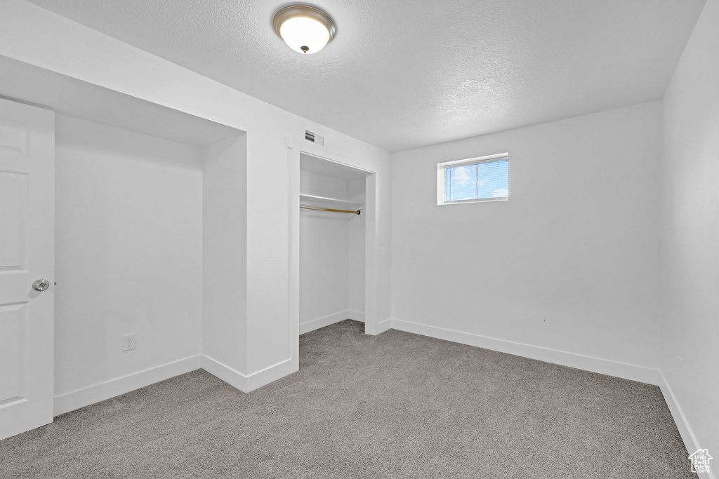 Unfurnished bedroom featuring a textured ceiling, carpet flooring, baseboards, and a closet