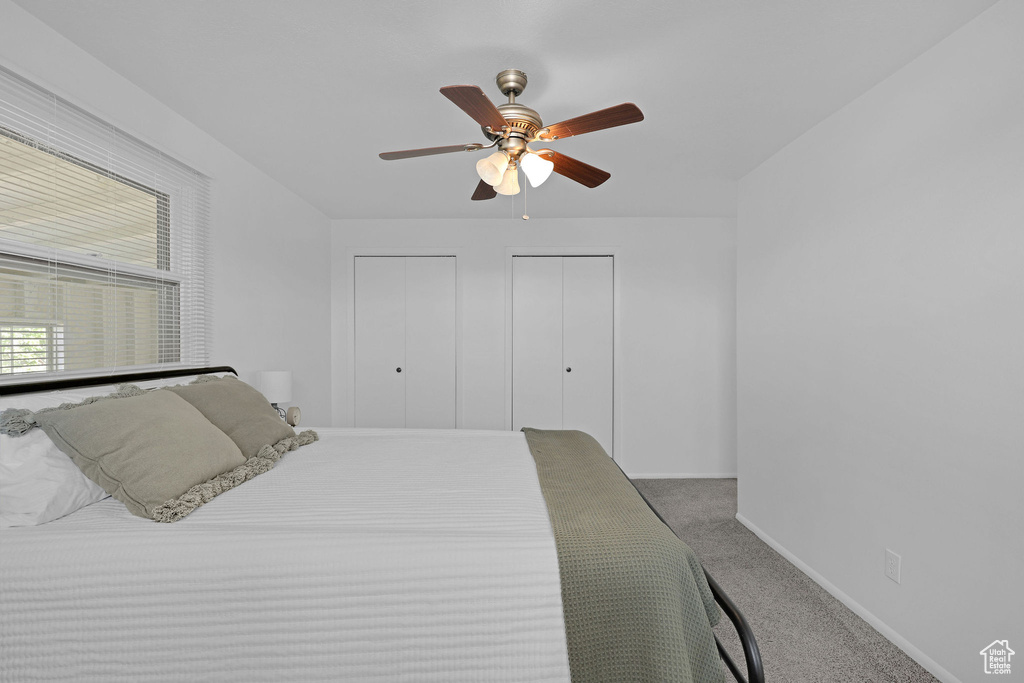 Carpeted bedroom with multiple closets, baseboards, and a ceiling fan