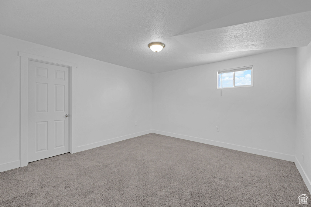 Carpeted empty room featuring a textured ceiling and baseboards