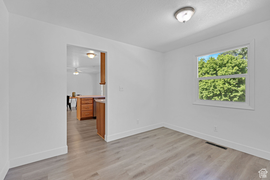 Unfurnished room featuring baseboards, light wood-type flooring, and a textured ceiling