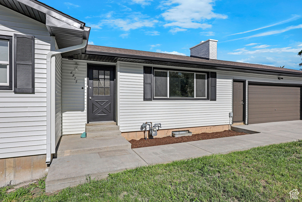 Property entrance with an attached garage, a chimney, concrete driveway, and a shingled roof
