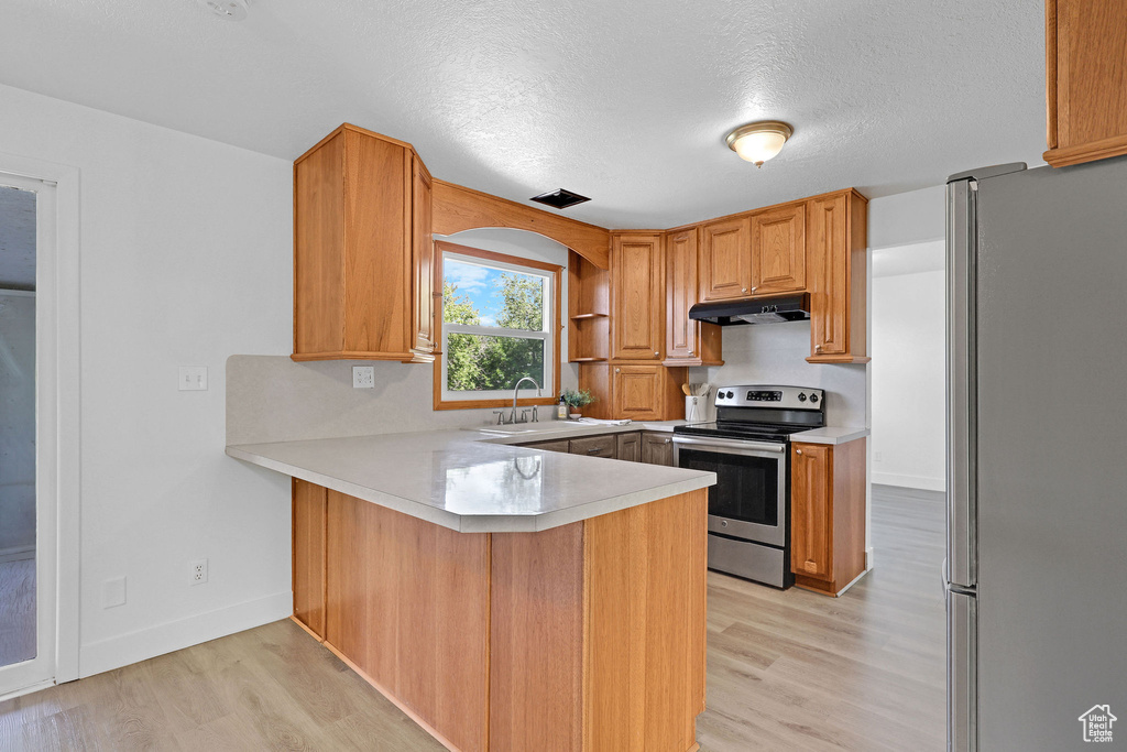 Kitchen featuring appliances with stainless steel finishes, under cabinet range hood, a peninsula, light wood-style flooring, and light countertops