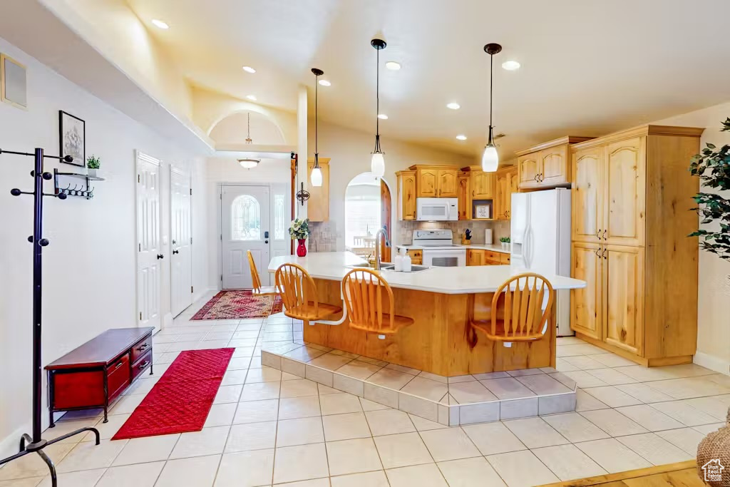 Kitchen featuring white appliances, light countertops, a sink, a peninsula, and pendant lighting
