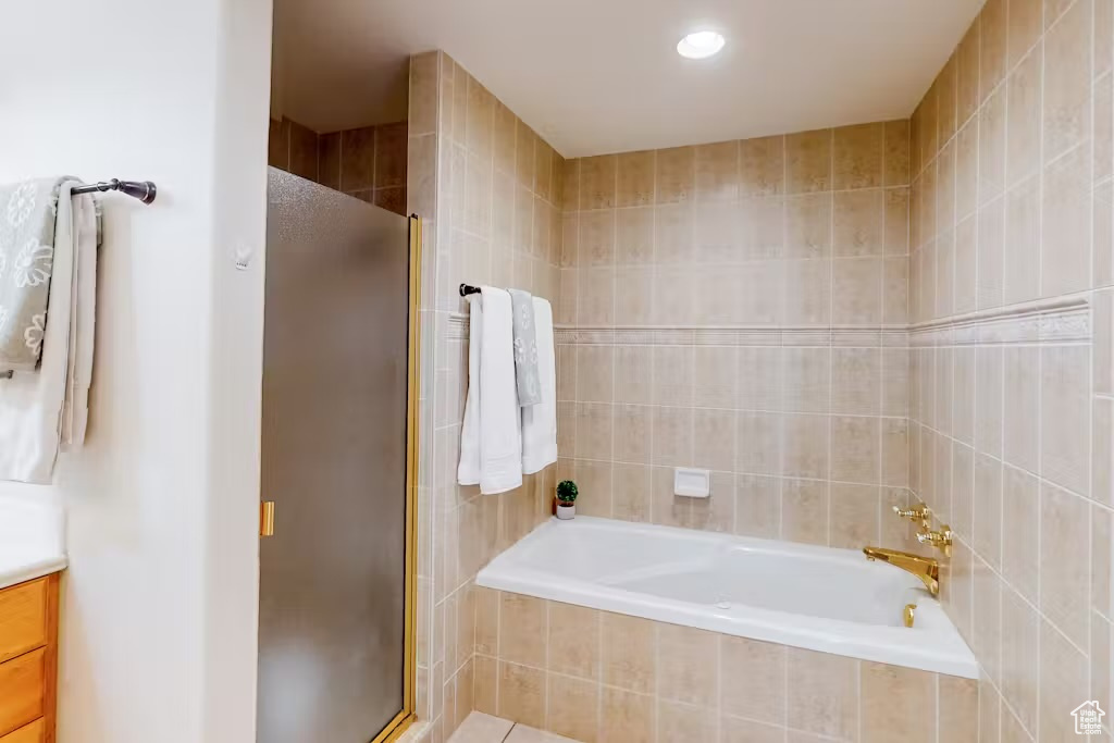 Bathroom with a stall shower, vanity, a garden tub, tile walls, and recessed lighting
